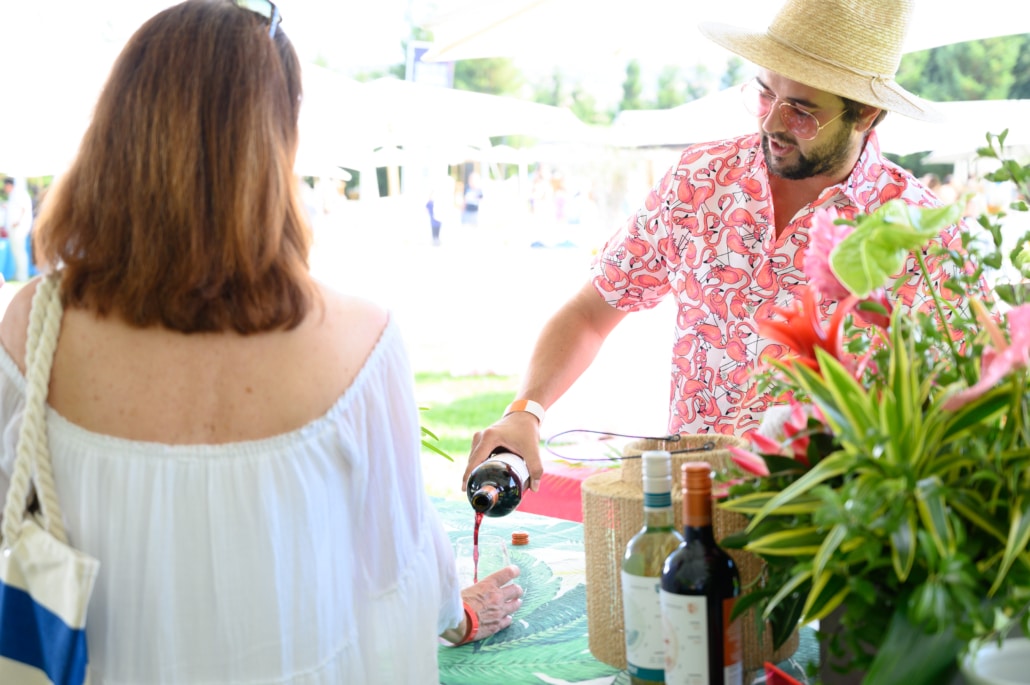 Man in a flamingo shirt and hat pouring wine for a woman